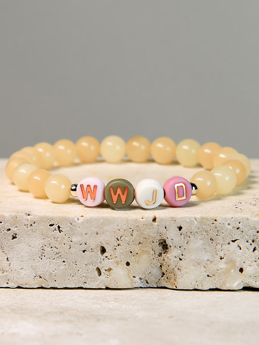 Angled product shot of the Golden Grace WWJD Bracelet resting on a textured stone block, highlighting the cheerful color palette and Christian message.