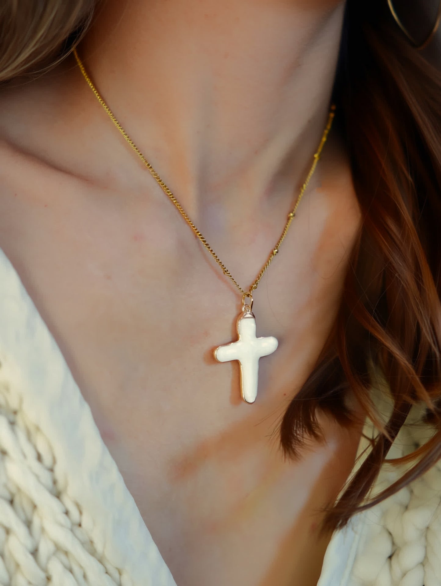Model Woman wearing a white shell cross necklace layered with gold chains – faith-based jewelry styled with a boho blouse.
