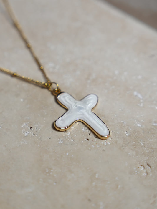 Artistic close-up of a white shell cross necklace resting on a travertine surface – handcrafted spiritual pendant in natural light.