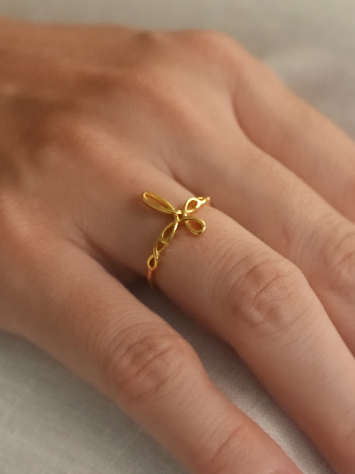 Gold sculptural cross ring on hand, viewed from side angle to emphasize the twisted ribbon design