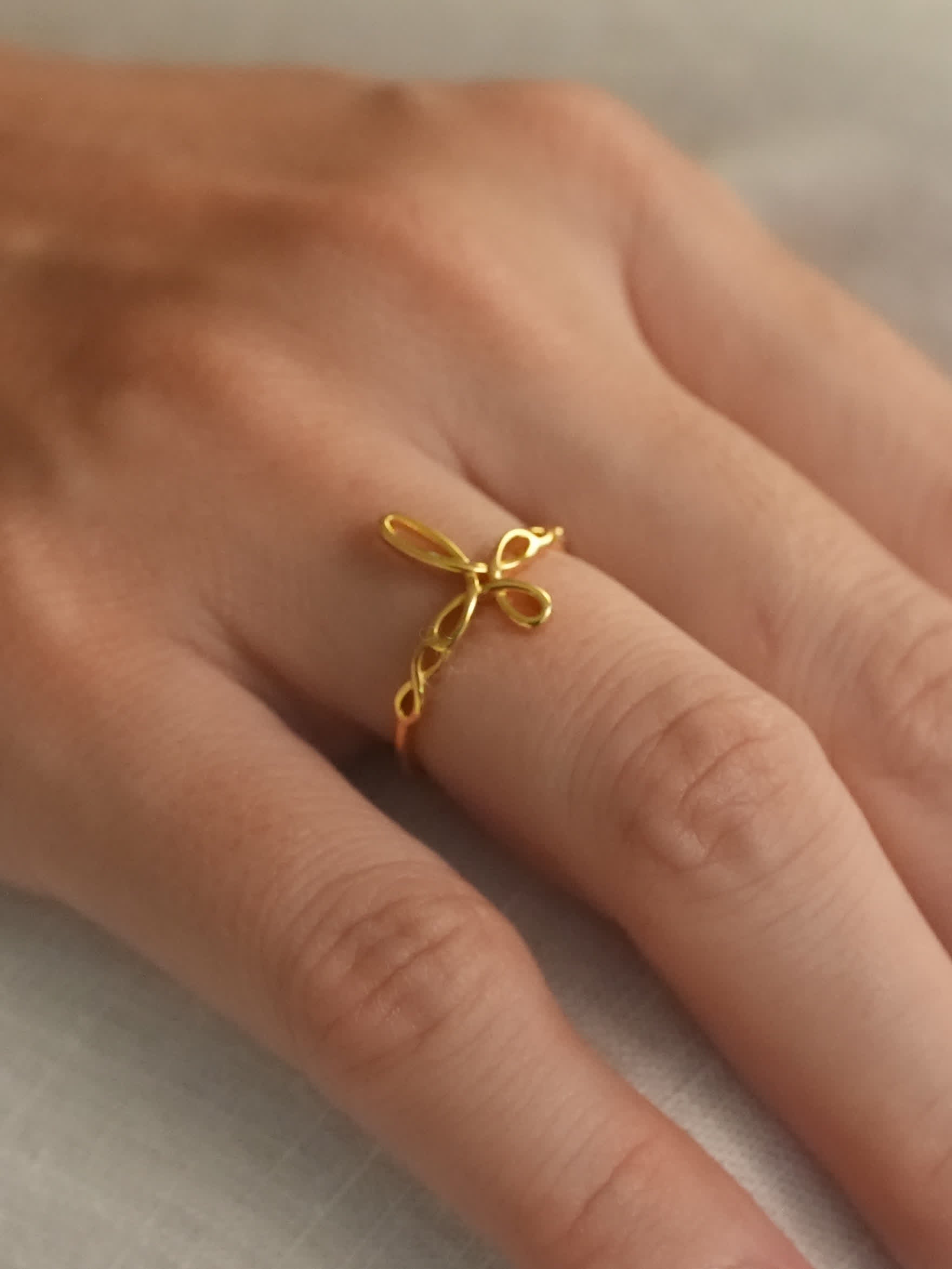 Gold sculptural cross ring on hand, viewed from side angle to emphasize the twisted ribbon design