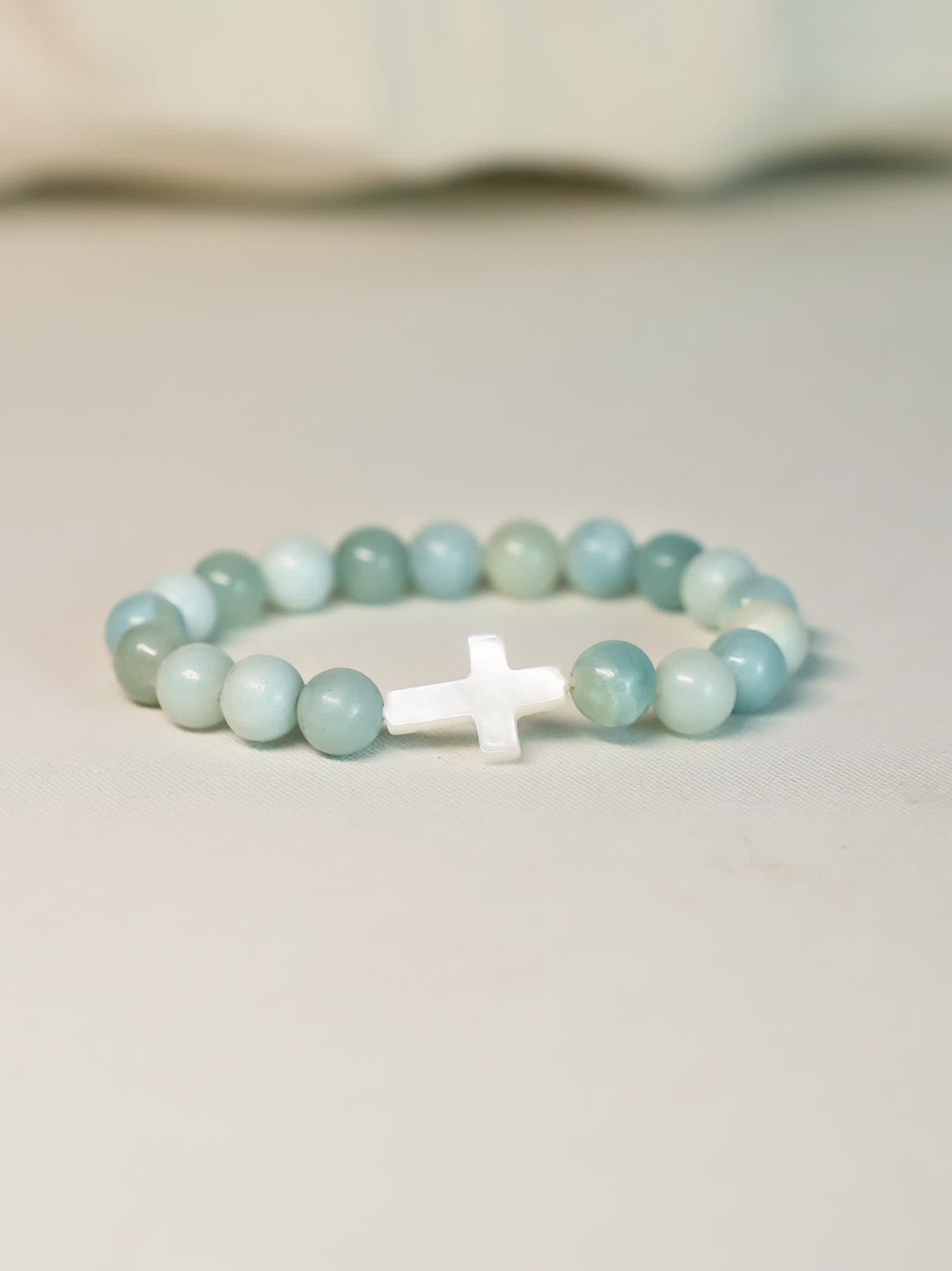 Front-facing product shot of the Sea of Grace Cross Bracelet on a clean neutral background, showcasing the cross and ocean-toned gemstone beads.