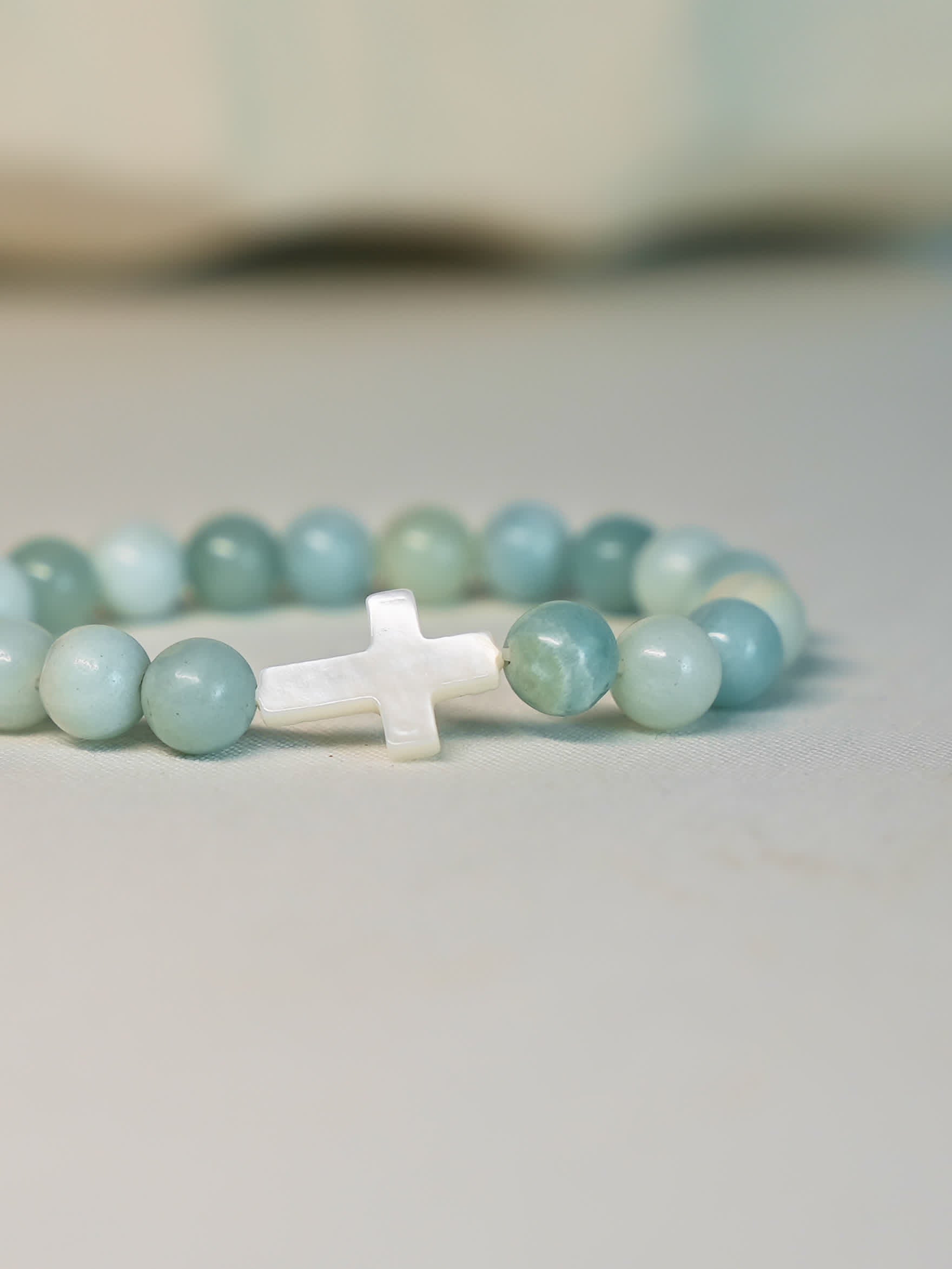 Angled image of the Sea of Grace Cross Bracelet with a slight shadow, highlighting the glossy finish of the Amazonite beads and the brightness of the shell cross.