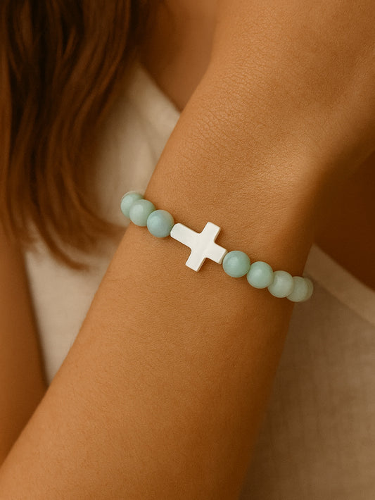 Lifestyle image of the Sea of Grace Cross Bracelet worn on a woman’s wrist, featuring soft green Amazonite beads and a central white shell cross.