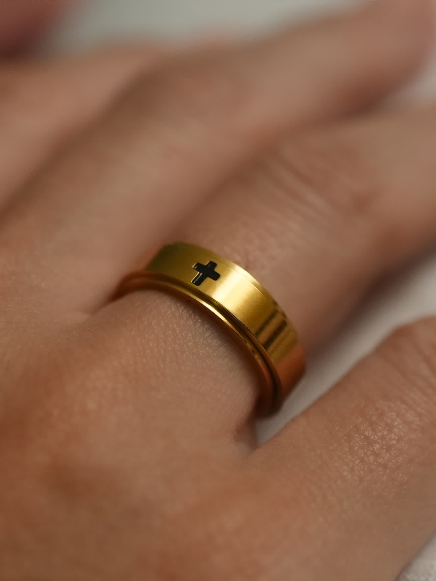 Gold cross spinner ring on male hand, reflecting polished 18K gold with subtle rotation