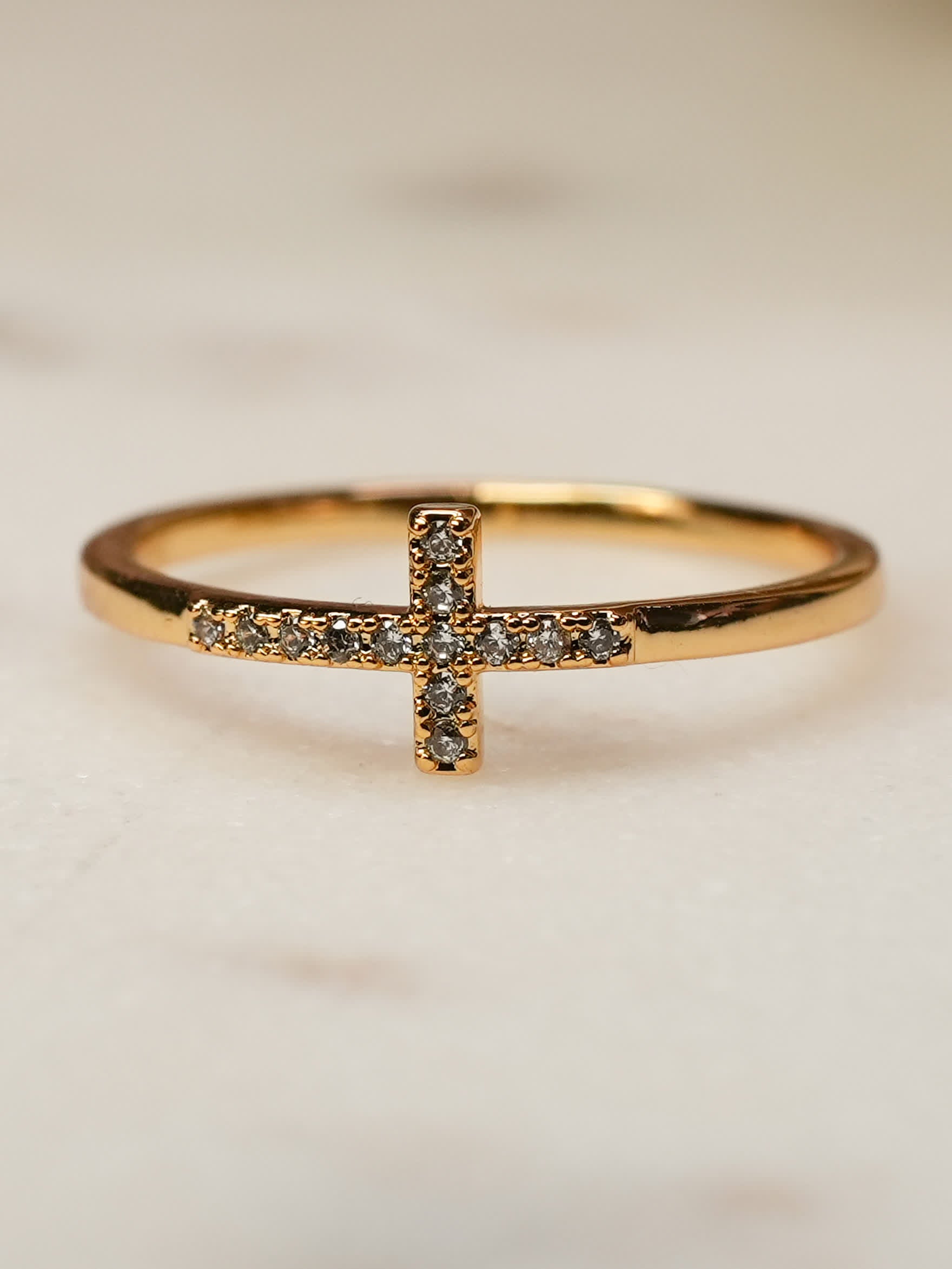 Side angle of the Anointed Radiance ring on a soft background, emphasizing the curved gold band and radiant pavé cross