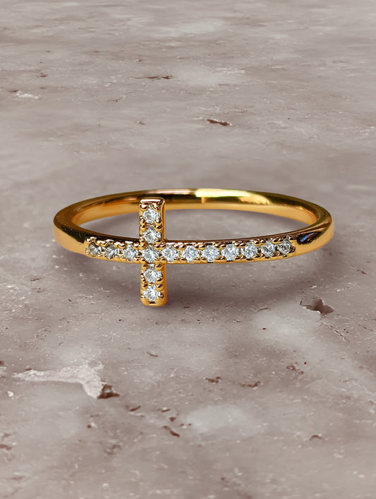 Close-up of the gold cross ring resting on a marble surface, showcasing the sparkle of its crystal-inlaid cross
