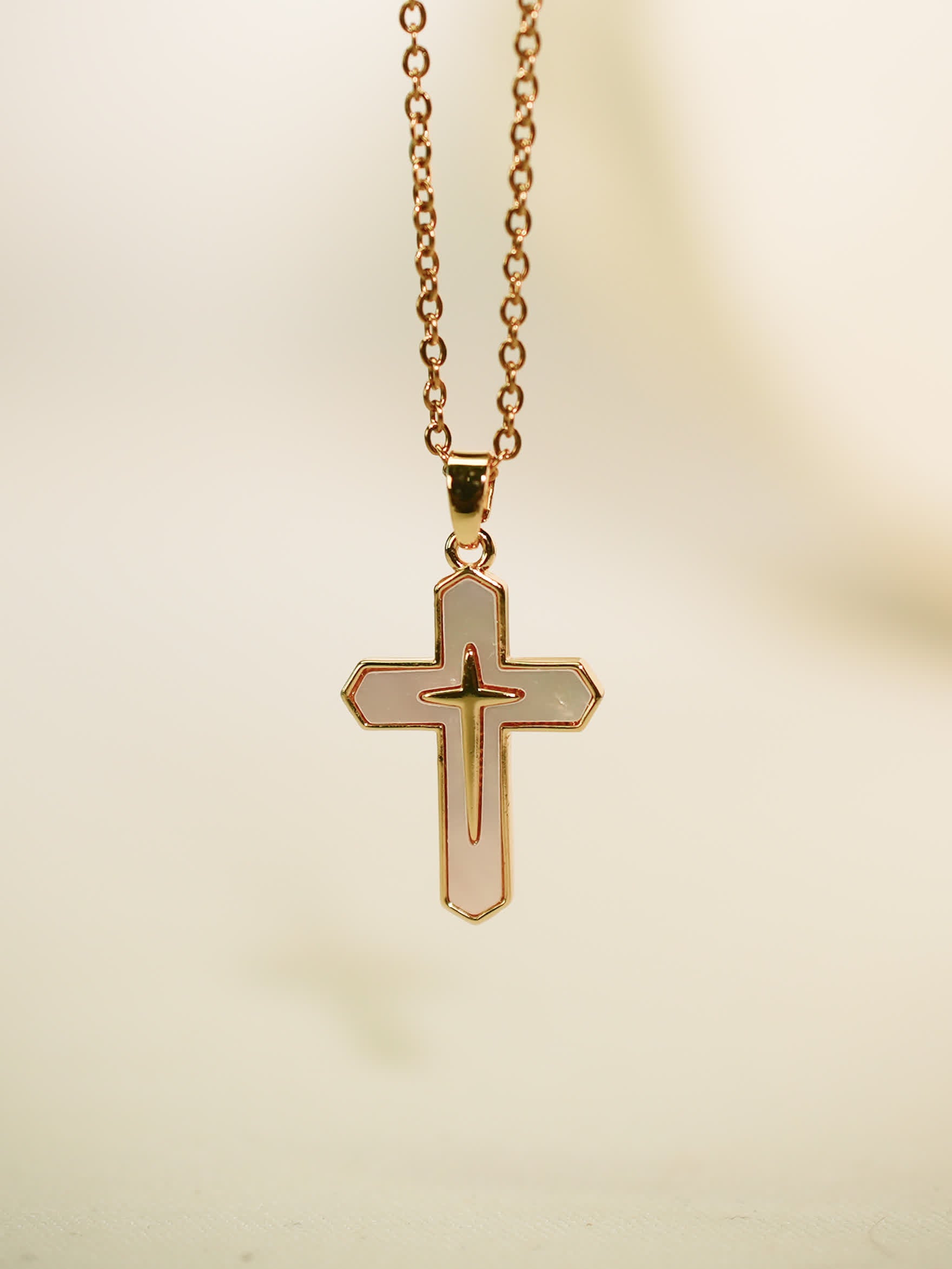 Vertical studio image of the gold enamel cross pendant hanging against a soft neutral backdrop