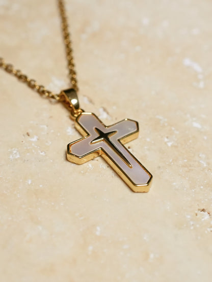 Gold and white cross necklace resting on a textured beige stone surface