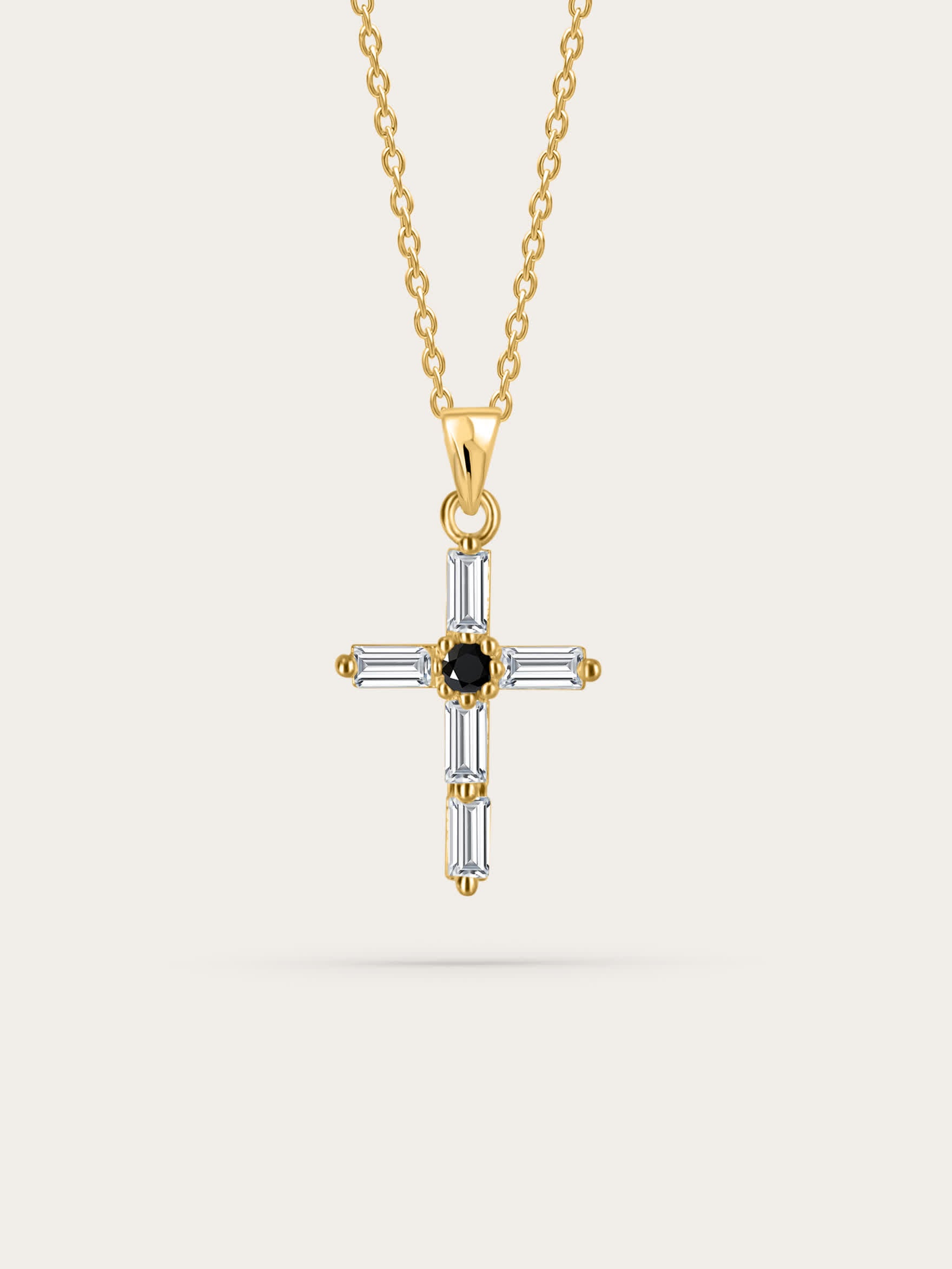 Studio shot of crystal cross necklace — A front-facing product photo of a gold cross necklace featuring baguette-cut clear crystals and a black center stone, against a clean cream background.