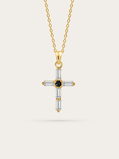 Studio shot of crystal cross necklace — A front-facing product photo of a gold cross necklace featuring baguette-cut clear crystals and a black center stone, against a clean cream background.