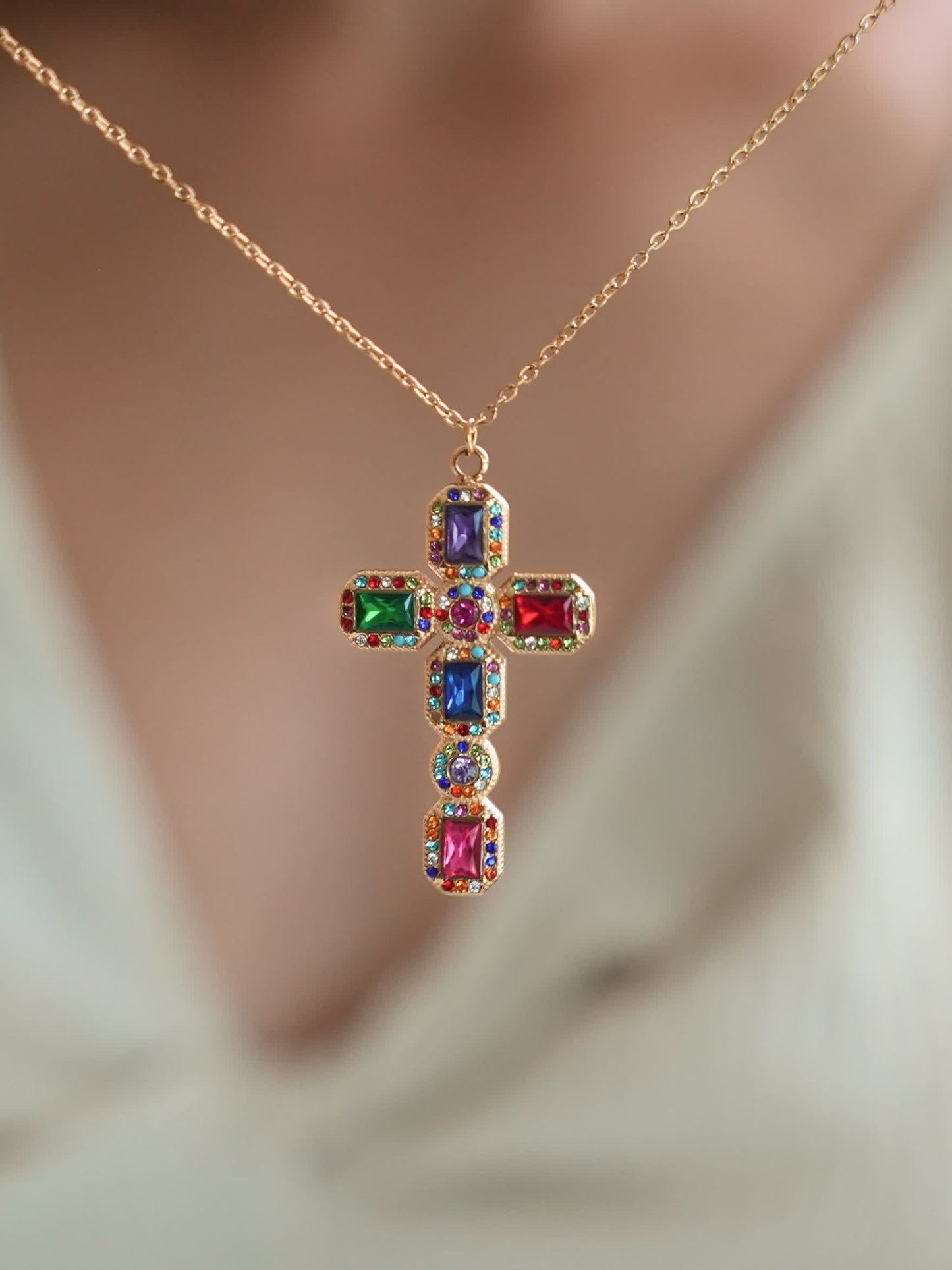 Baroque multistone cross pendant worn by a model in a v-neck white top, highlighting the bold and colorful gemstone arrangement with elegant 18K gold detailing.