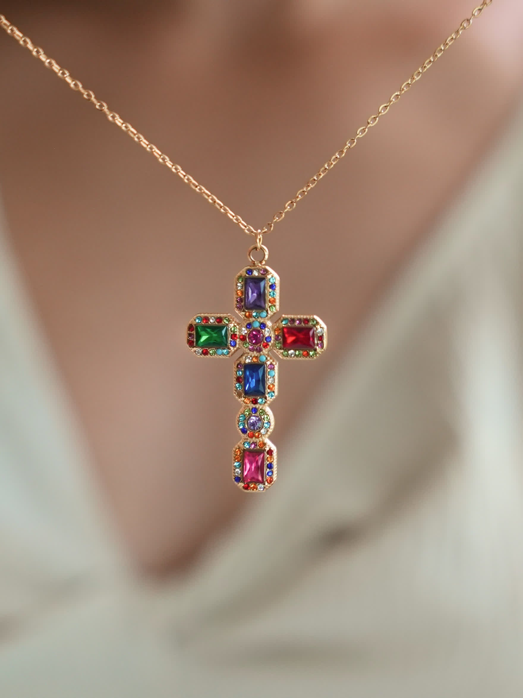 Baroque multistone cross pendant worn by a model in a v-neck white top, highlighting the bold and colorful gemstone arrangement with elegant 18K gold detailing.
