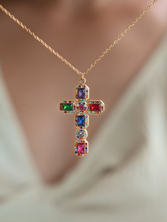 Baroque multistone cross pendant worn by a model in a v-neck white top, highlighting the bold and colorful gemstone arrangement with elegant 18K gold detailing.