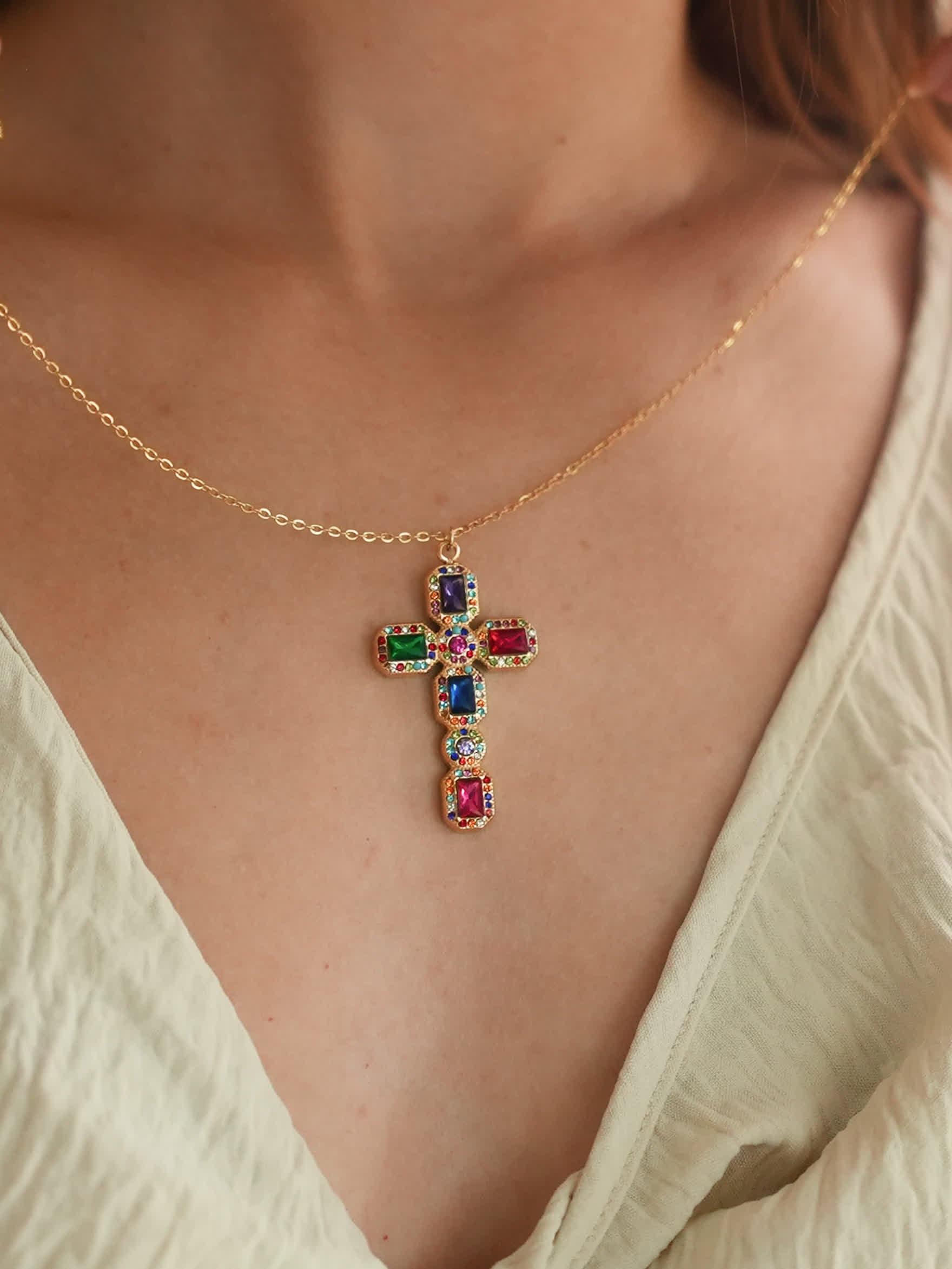 Baroque jeweled cross necklace resting on a model’s chest in a cream outfit, showcasing the spiritual elegance and bright multicolor design in natural light.