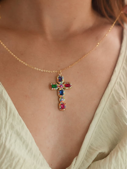 Baroque jeweled cross necklace resting on a model’s chest in a cream outfit, showcasing the spiritual elegance and bright multicolor design in natural light.