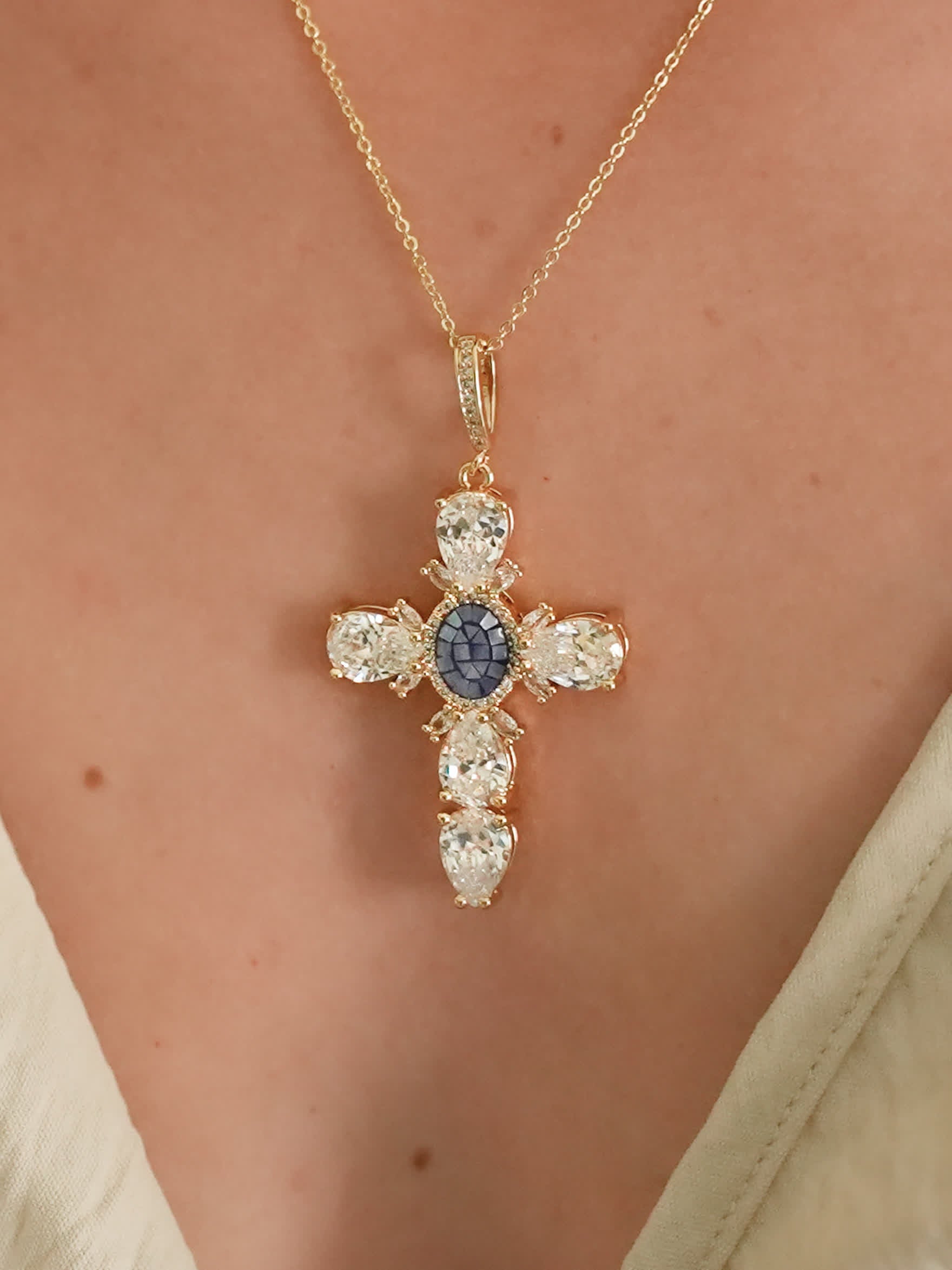 Blue gemstone and crystal cross necklace worn on a woman's chest, showcasing the necklace's size and shine against skin