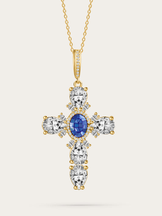 Elegant gold cathedral cross necklace featuring a royal blue oval gemstone and teardrop-shaped white crystals, displayed on a white background