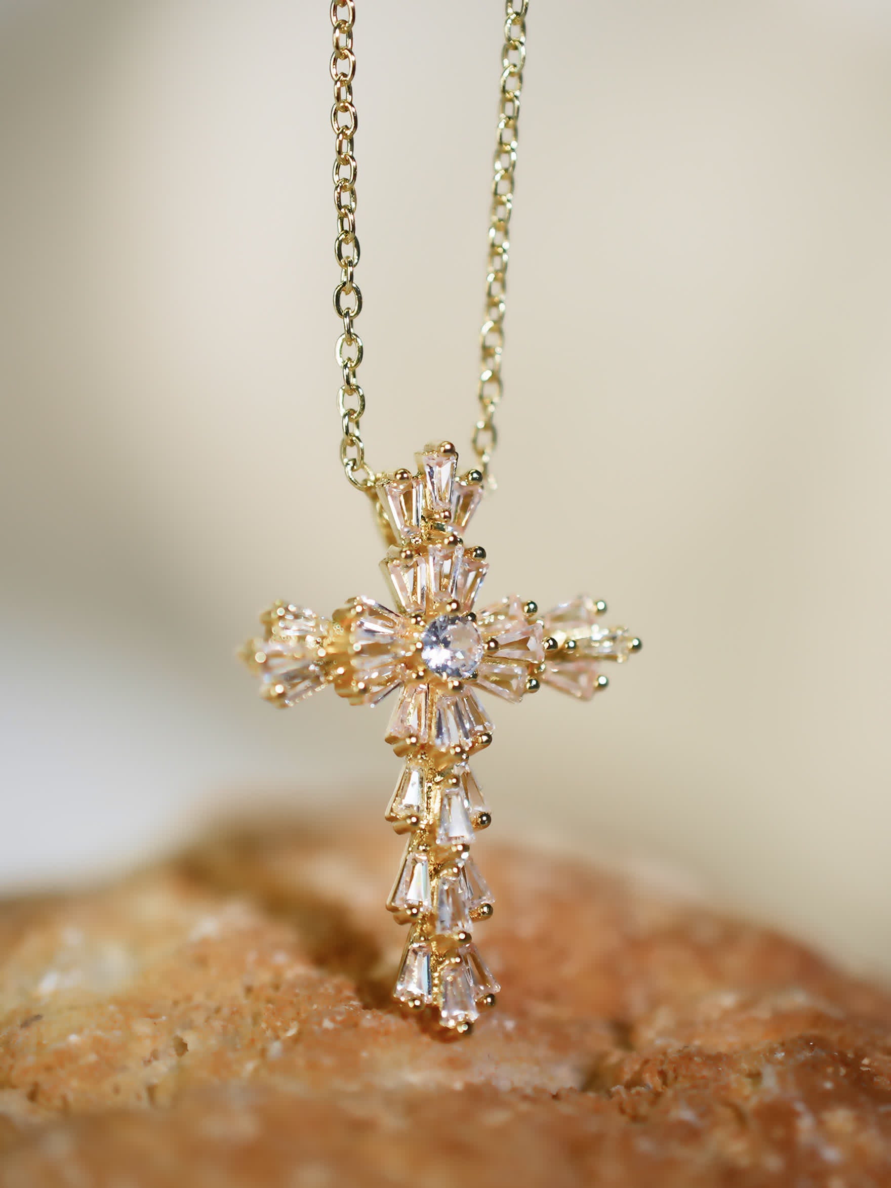 Golden crystal cross pendant displayed on a peachy stone surface, emphasizing floral zircon arrangement and shine