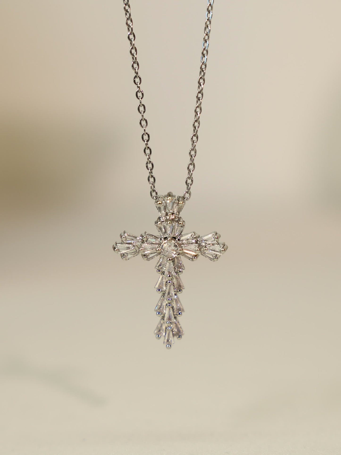 Hanging pendant view: Vertical shot of the silver cross necklace hanging, showcasing teardrop and baguette zircon detail