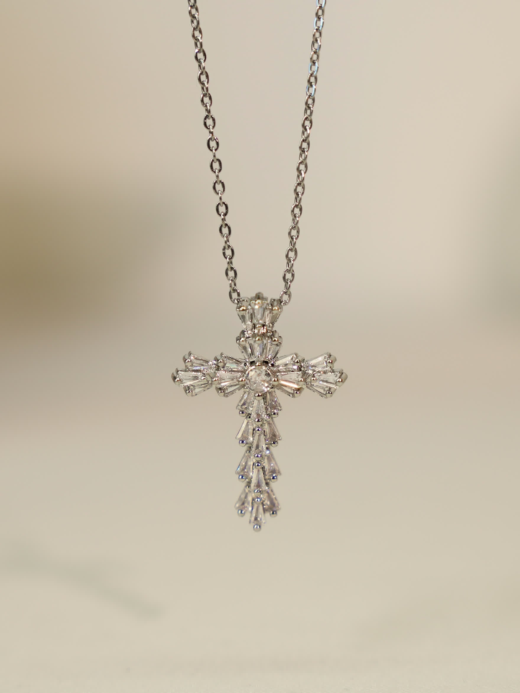Hanging pendant view: Vertical shot of the silver cross necklace hanging, showcasing teardrop and baguette zircon detail