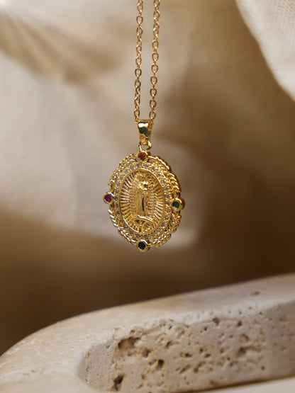 Gold Virgin Mary pendant necklace hanging over a beige stone surface with soft natural lighting