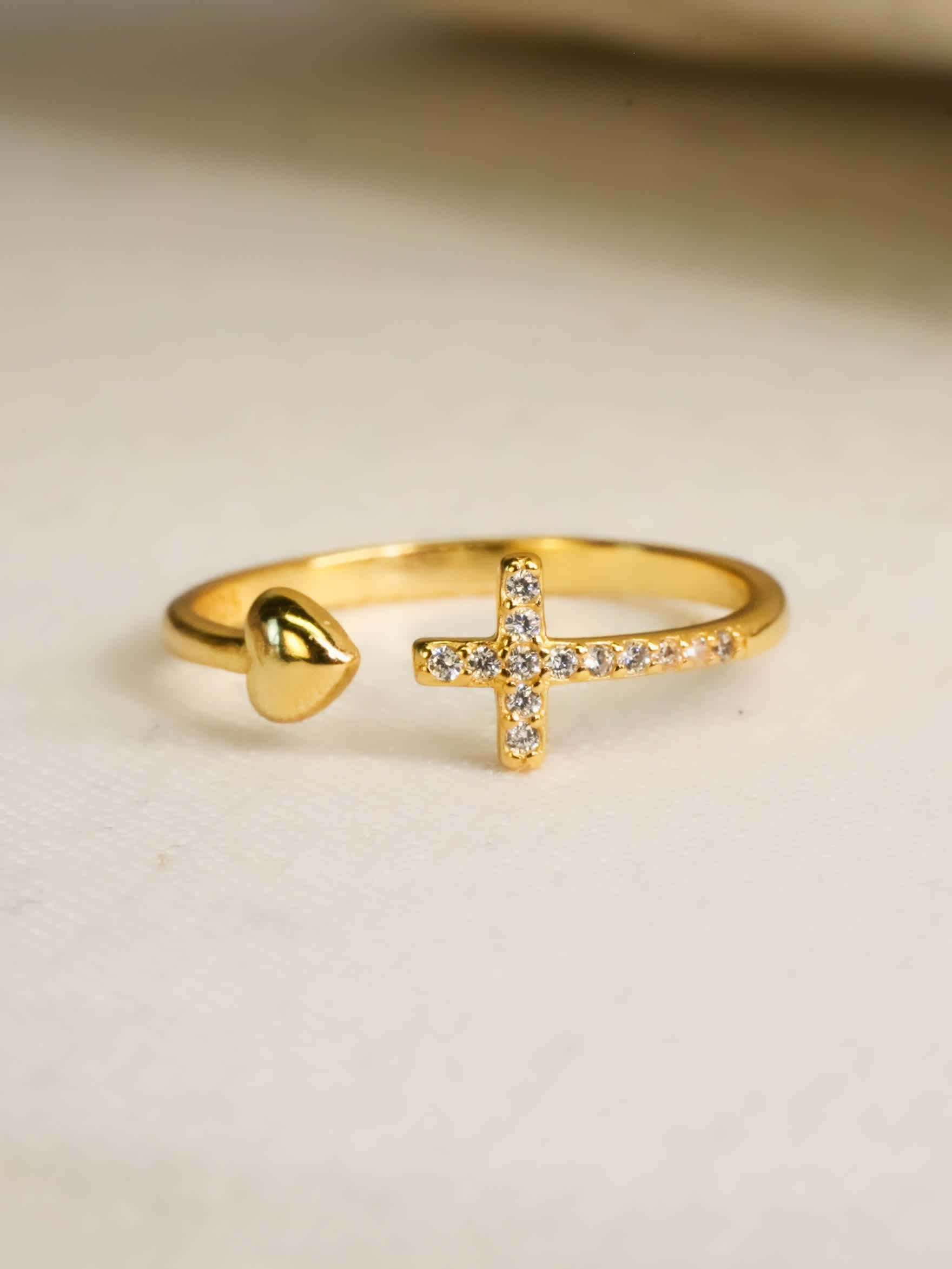Gold ring with a heart and cross design on a beige background