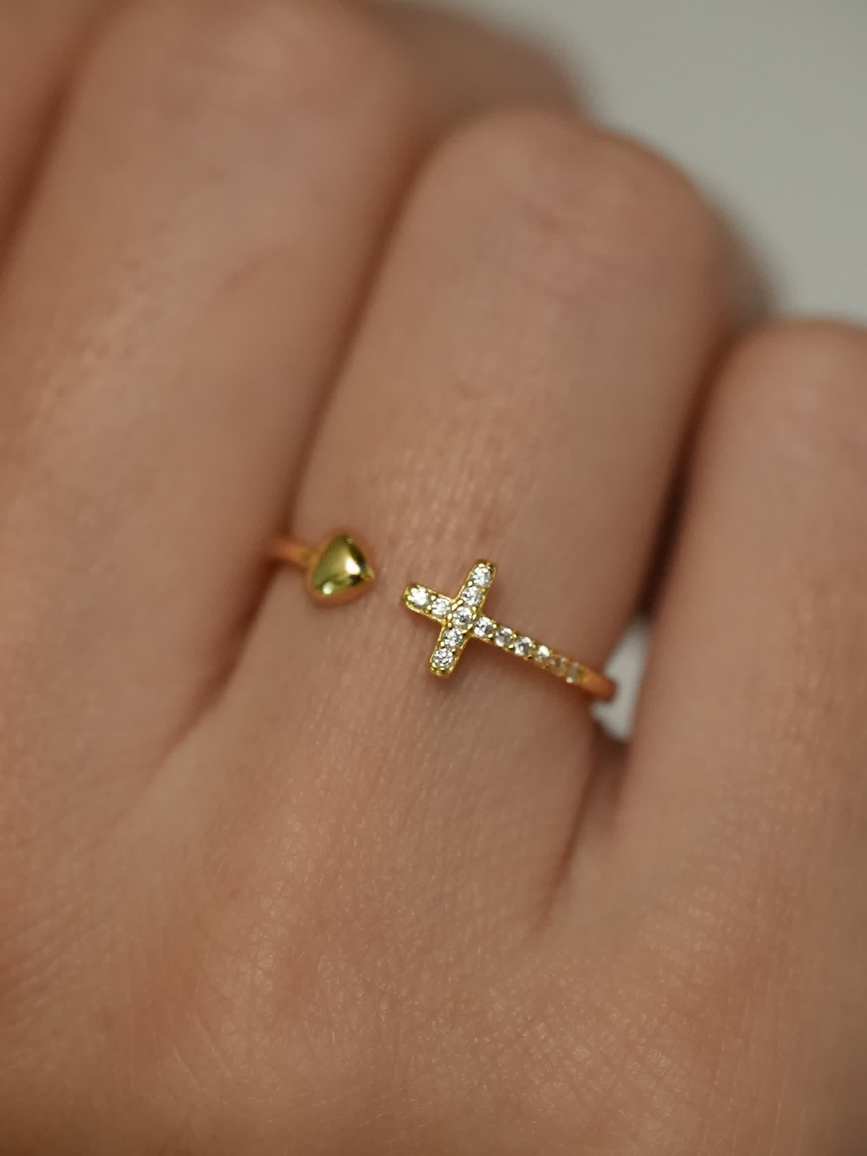 Gold ring with a heart and cross design on a finger