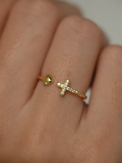 Gold ring with a heart and cross design on a finger