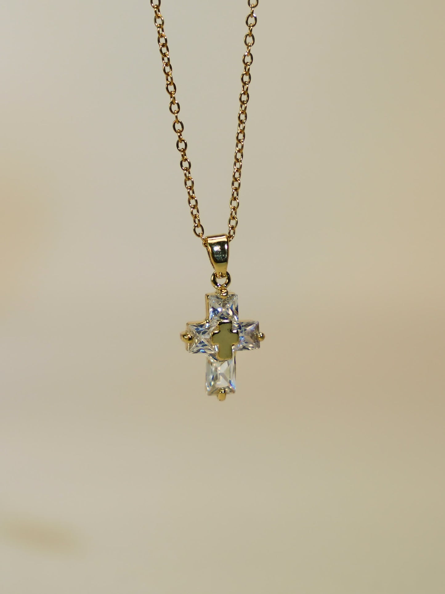 Product image of the gold and crystal cross necklace hanging freely against a soft ivory backdrop