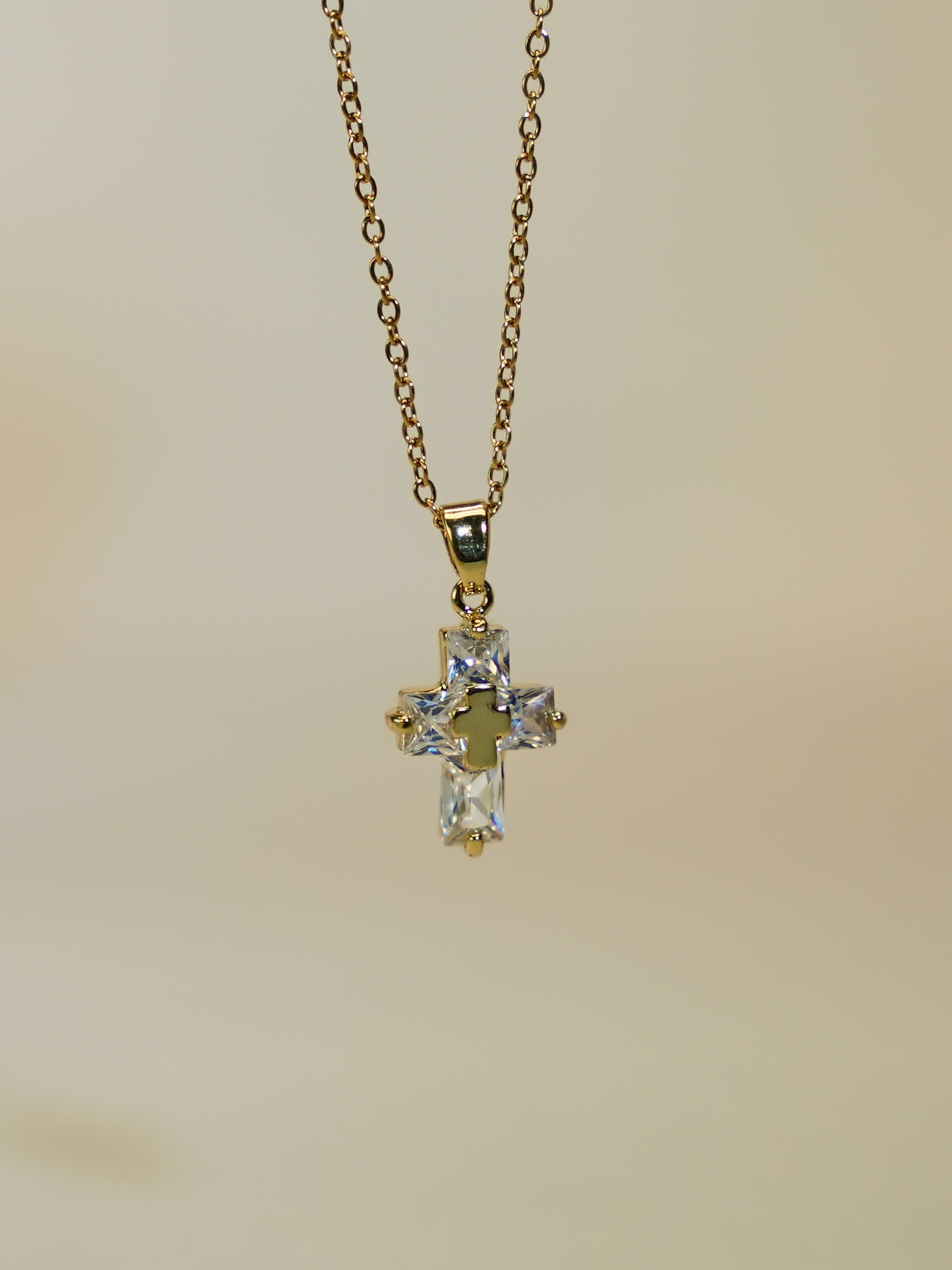 Product image of the gold and crystal cross necklace hanging freely against a soft ivory backdrop