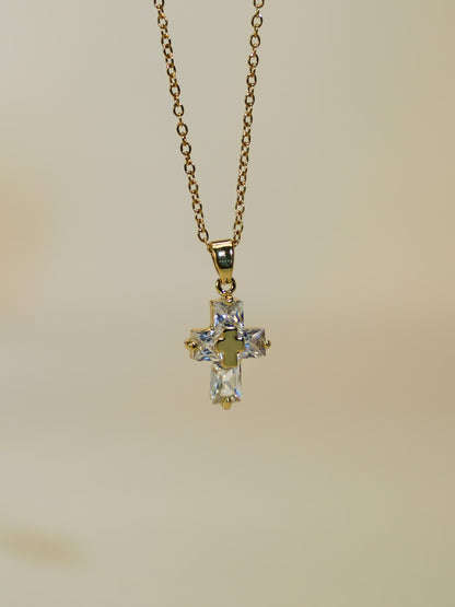 Product image of the gold and crystal cross necklace hanging freely against a soft ivory backdrop