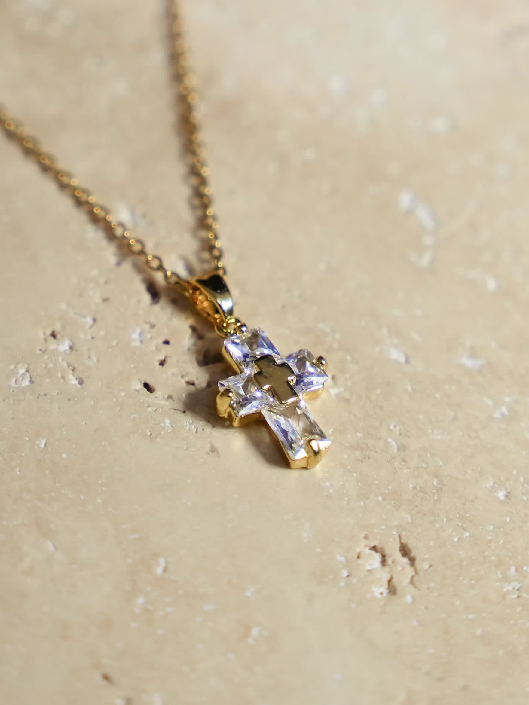 Artistic shot of the cross necklace on warm travertine stone with natural shadows and highlights