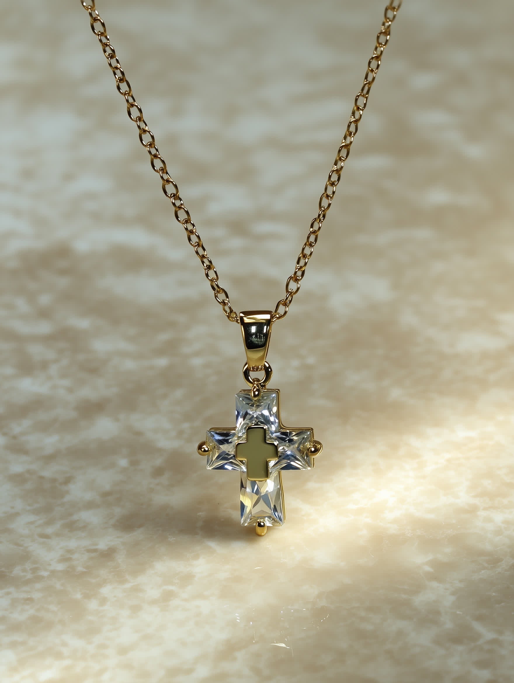 Close-up of the crystal cross necklace resting on a neutral surface, showing gold detailing and sparkling clear zircon stones