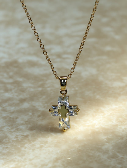 Close-up of the crystal cross necklace resting on a neutral surface, showing gold detailing and sparkling clear zircon stones