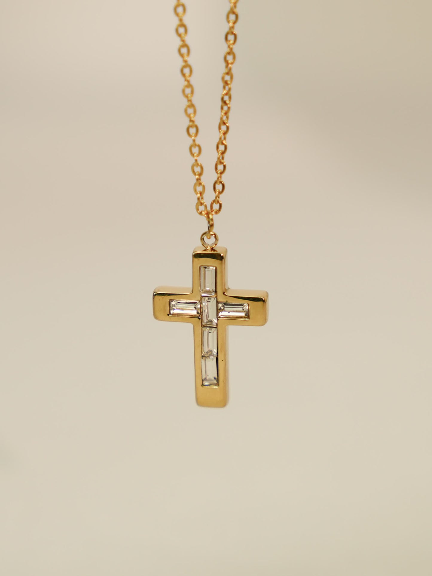 Close-up of gold vintage cross necklace with white zircon inlays on soft beige backdrop