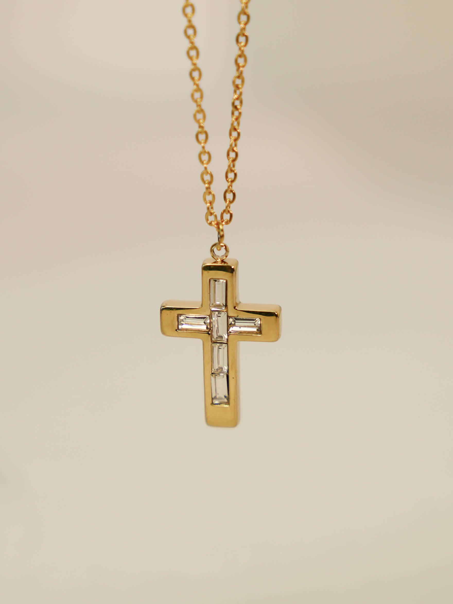 Close-up of gold vintage cross necklace with white zircon inlays on soft beige backdrop