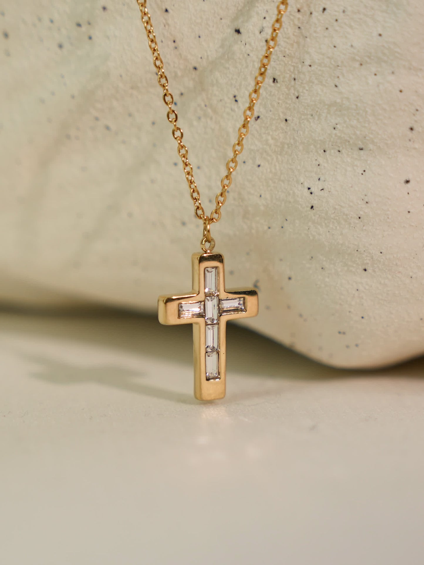 Faithline baguette cross pendant resting on light stone surface