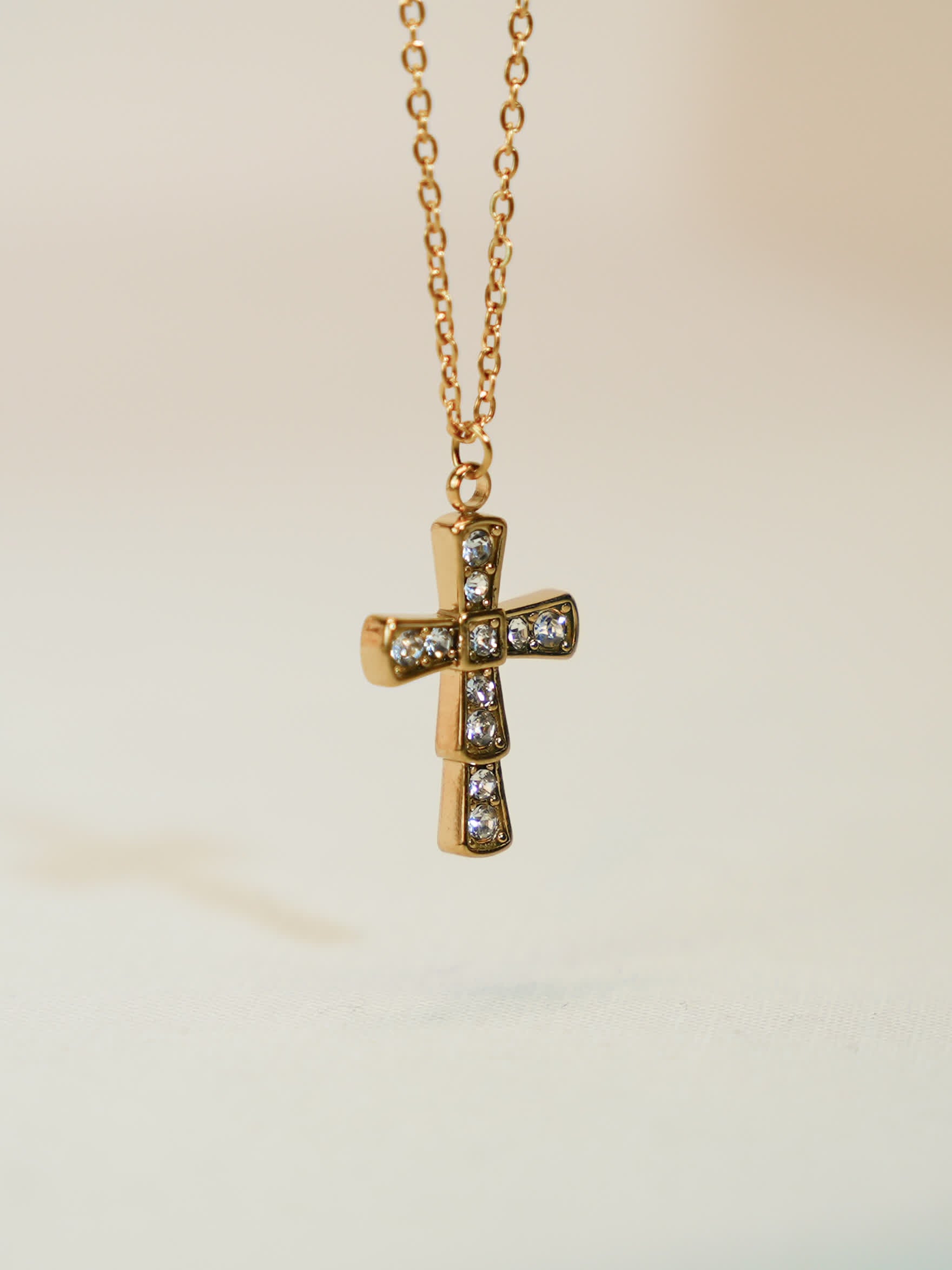 Elegant close-up of the gold cross pendant floating mid-air, highlighting the symmetry and shimmer of the crystals
