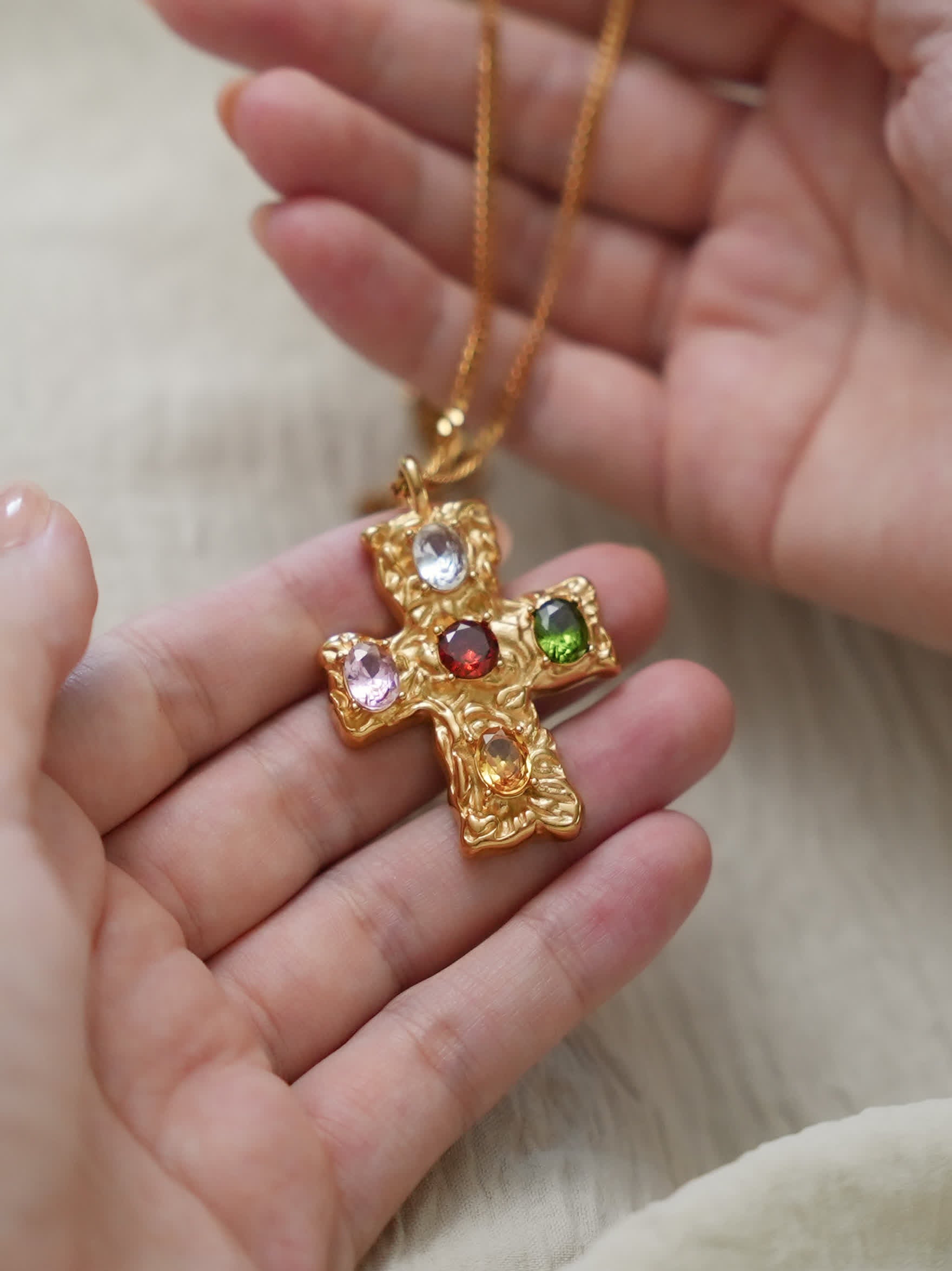 Hands holding radiant baroque-style multicolor Christian cross necklace in 18K gold