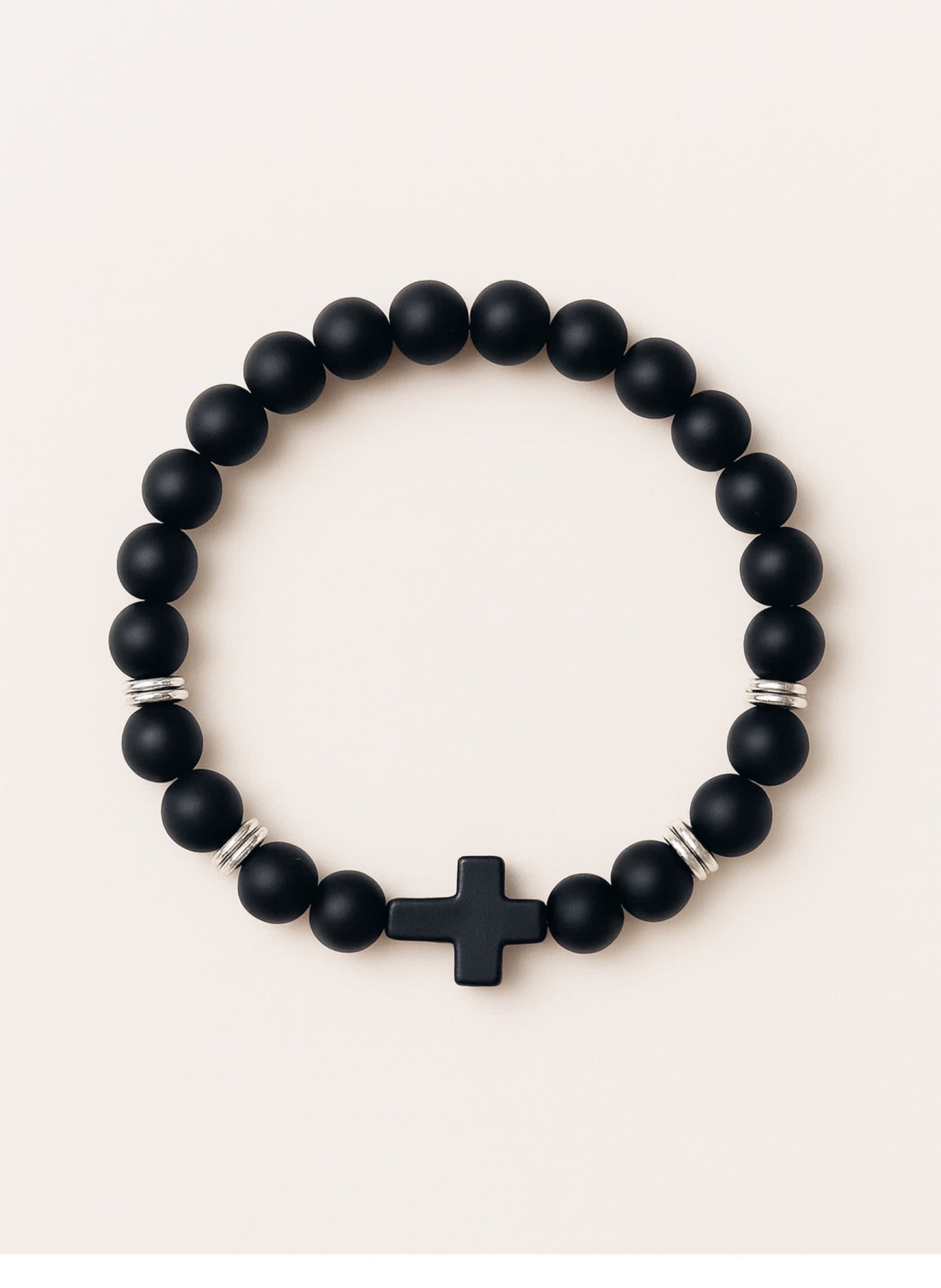 Studio product photo of the Covenant Shield Men's Cross Bracelet with matte black gemstone beads and a centered black cross, displayed against a soft cream background.