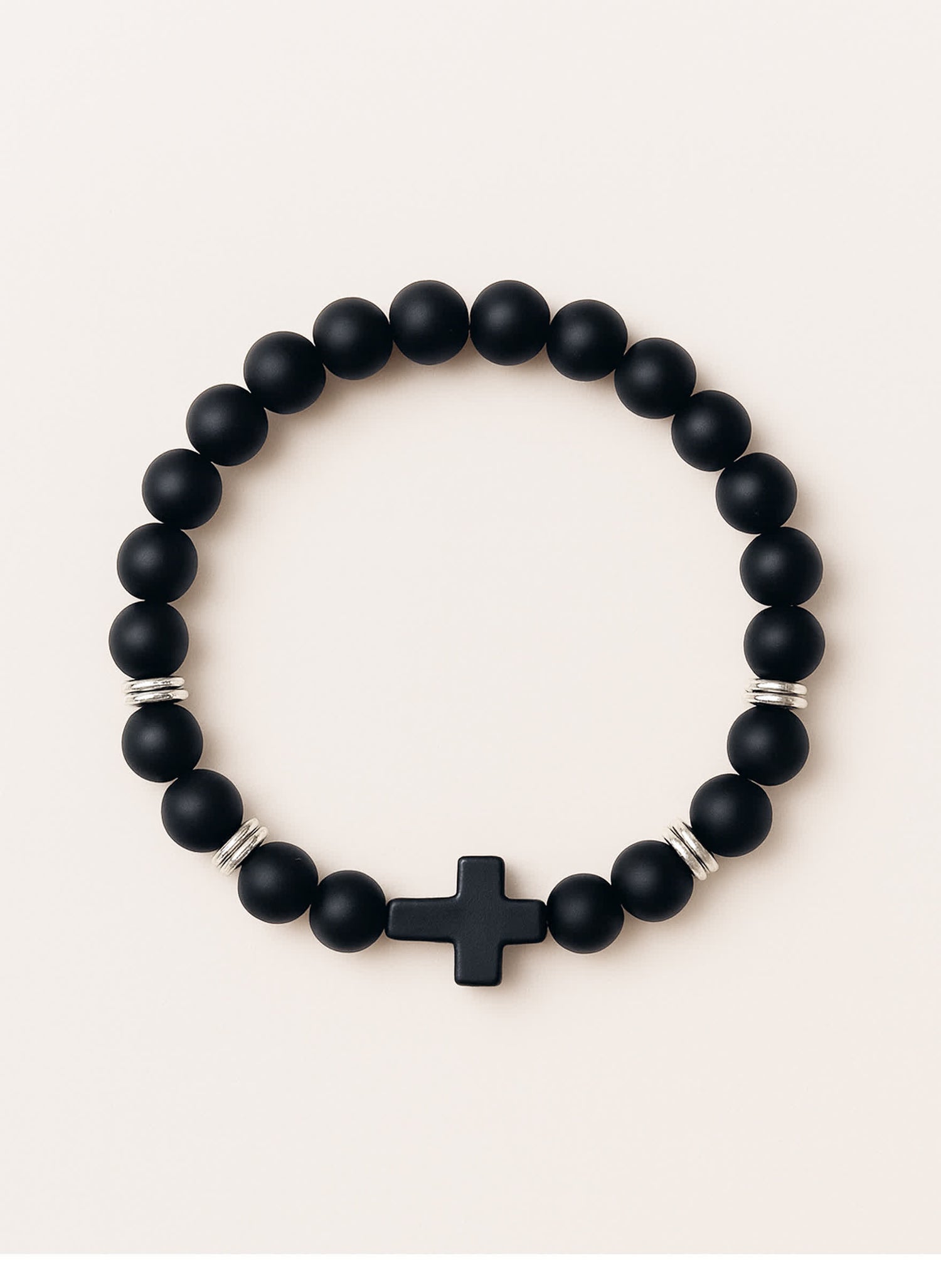 Studio product photo of the Covenant Shield Men's Cross Bracelet with matte black gemstone beads and a centered black cross, displayed against a soft cream background.