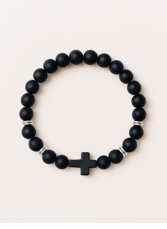 Studio product photo of the Covenant Shield Men's Cross Bracelet with matte black gemstone beads and a centered black cross, displayed against a soft cream background.