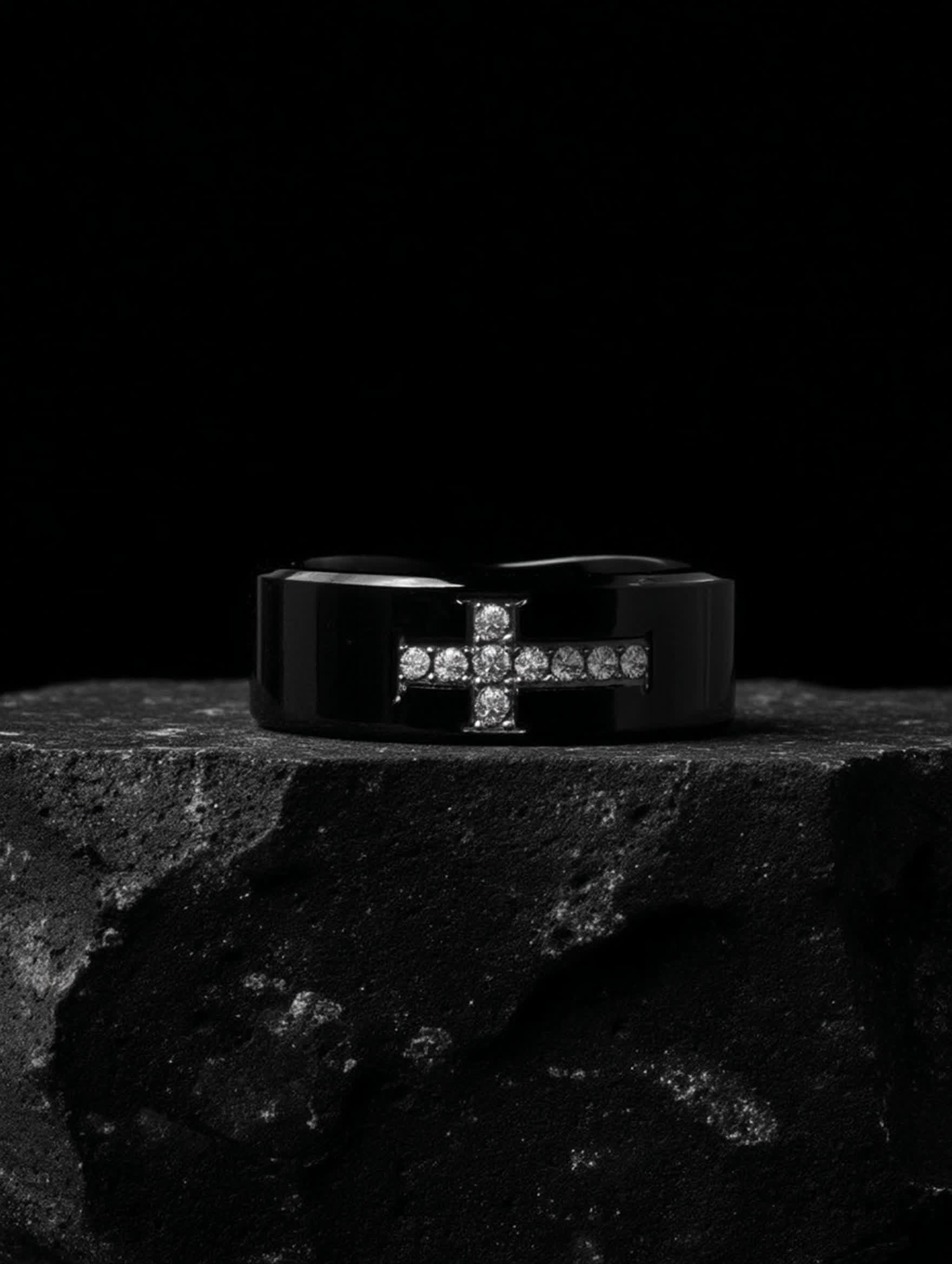 Angled view of Creed Noir Black Cross Ring displayed on rugged stone surface, capturing the masculine design and glossy black finish.