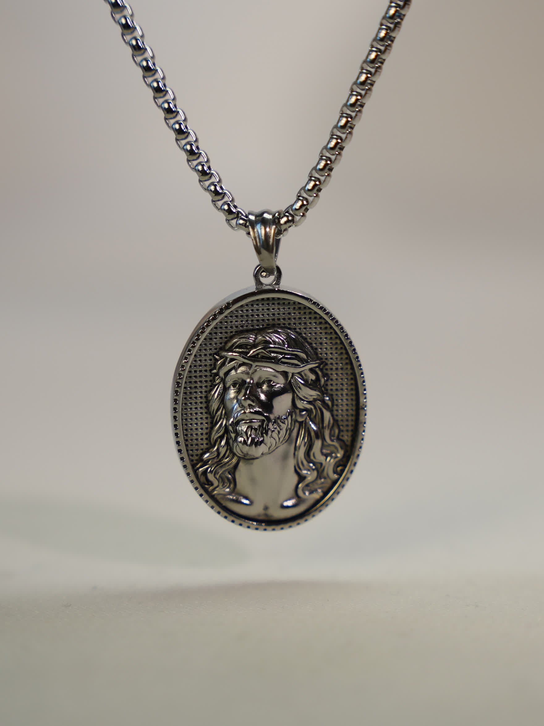 Close-up of oxidized silver Jesus pendant necklace resting upright on a soft neutral surface, highlighting the intricate sculpted detail.