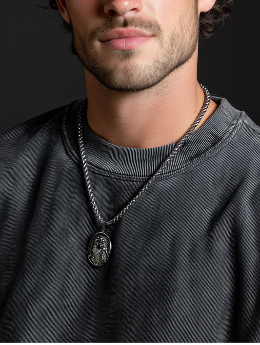 Man wearing stainless steel Jesus face necklace over a faded charcoal sweatshirt, showing modern masculine faith style.