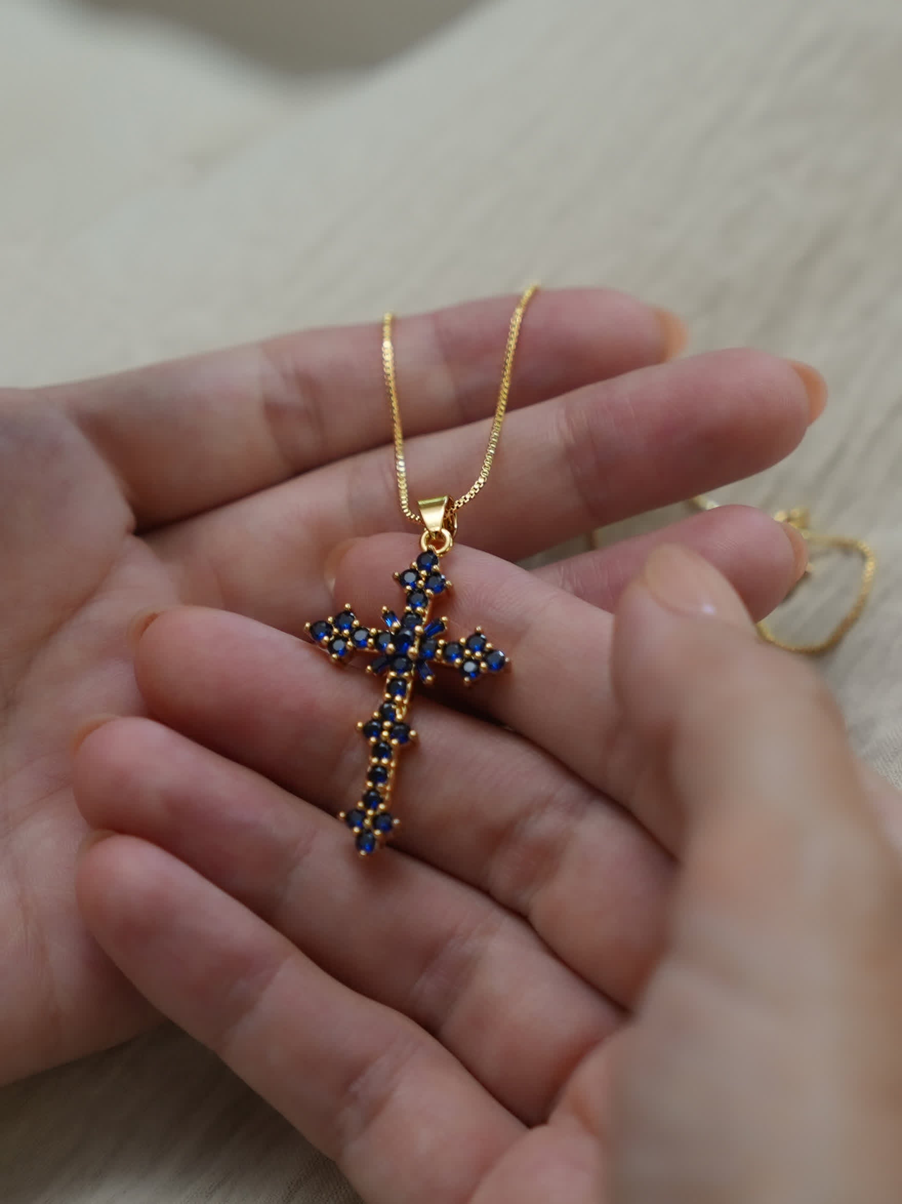 Artistic flat-lay of the blue crystal cross pendant on marble slab with warm natural lighting

Cropped shot of the necklace worn on model’s chest with soft depth of field, emphasizing elegance and clarity
