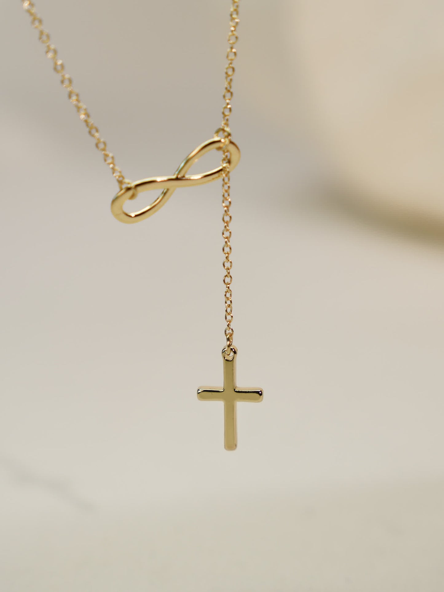 Side-hanging view of the necklace, emphasizing the floating cross suspended from the gold infinity loop
