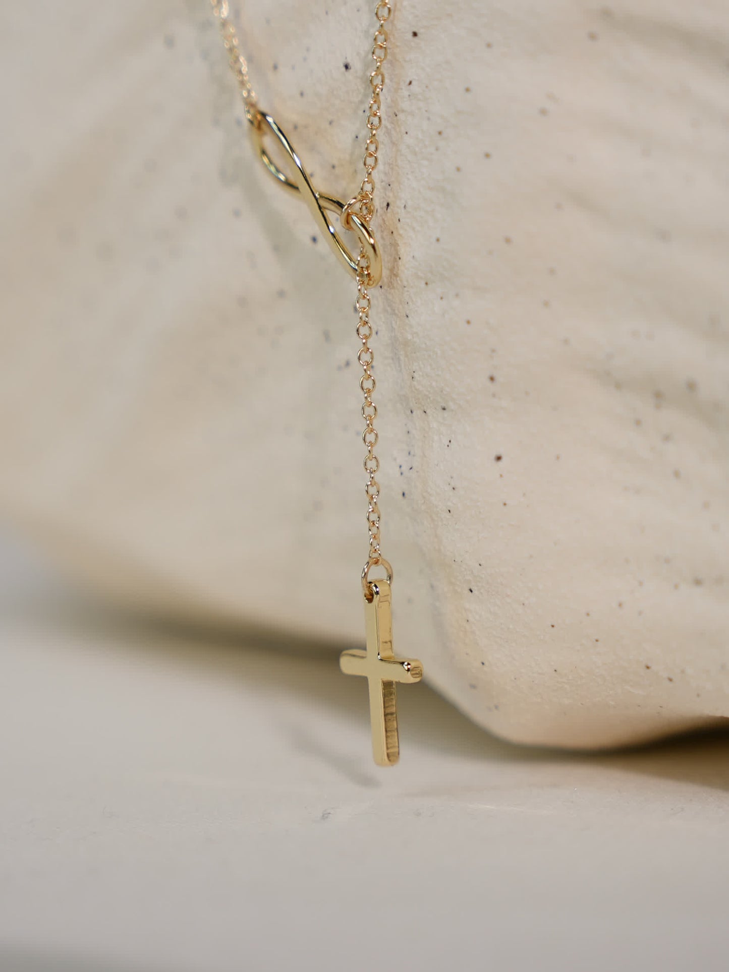 Detailed image of the necklace draped over a neutral stone surface, highlighting the polished gold-tone finish