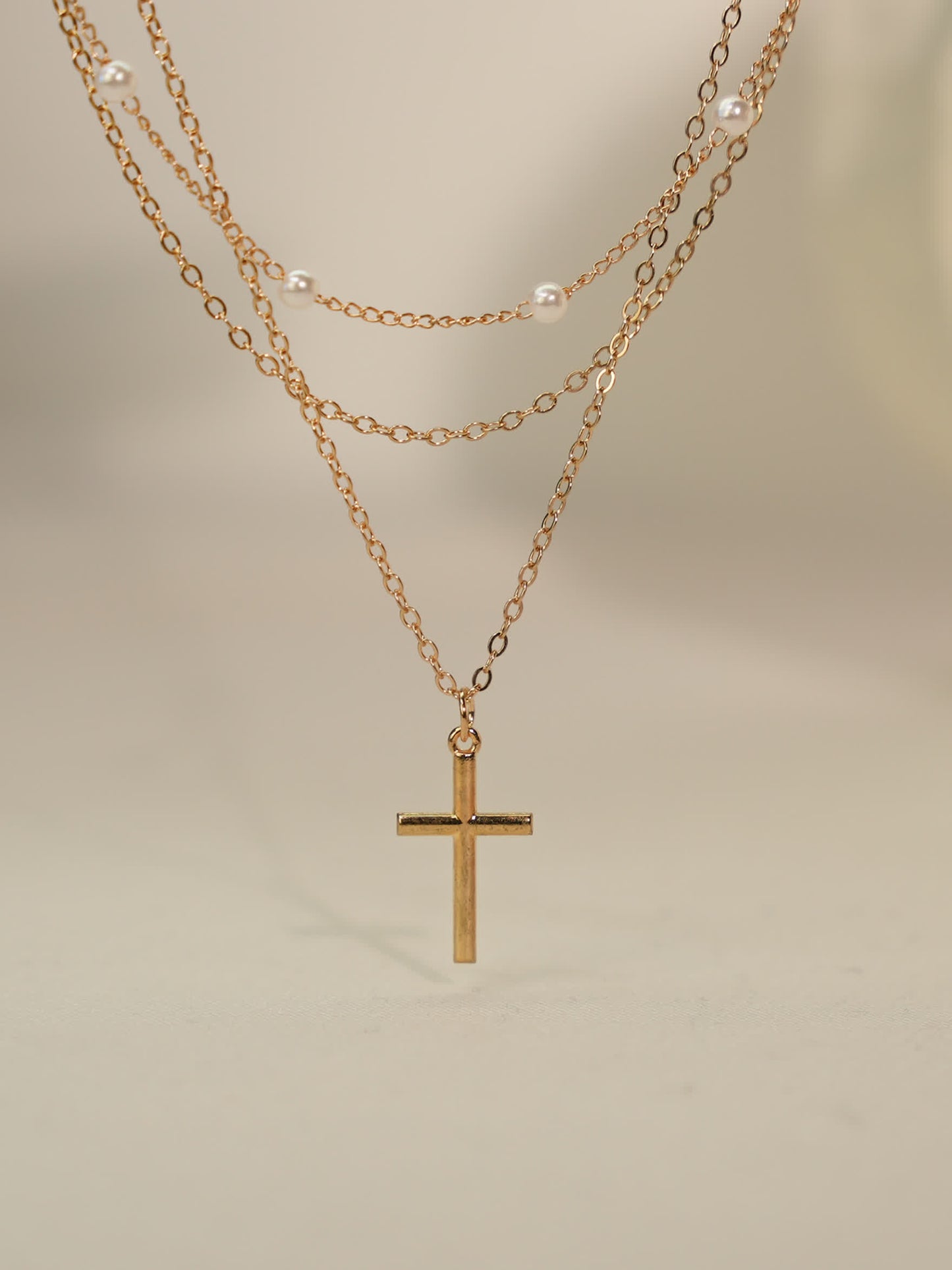 Minimalist pearl and cross necklace photographed on neutral stone backdrop